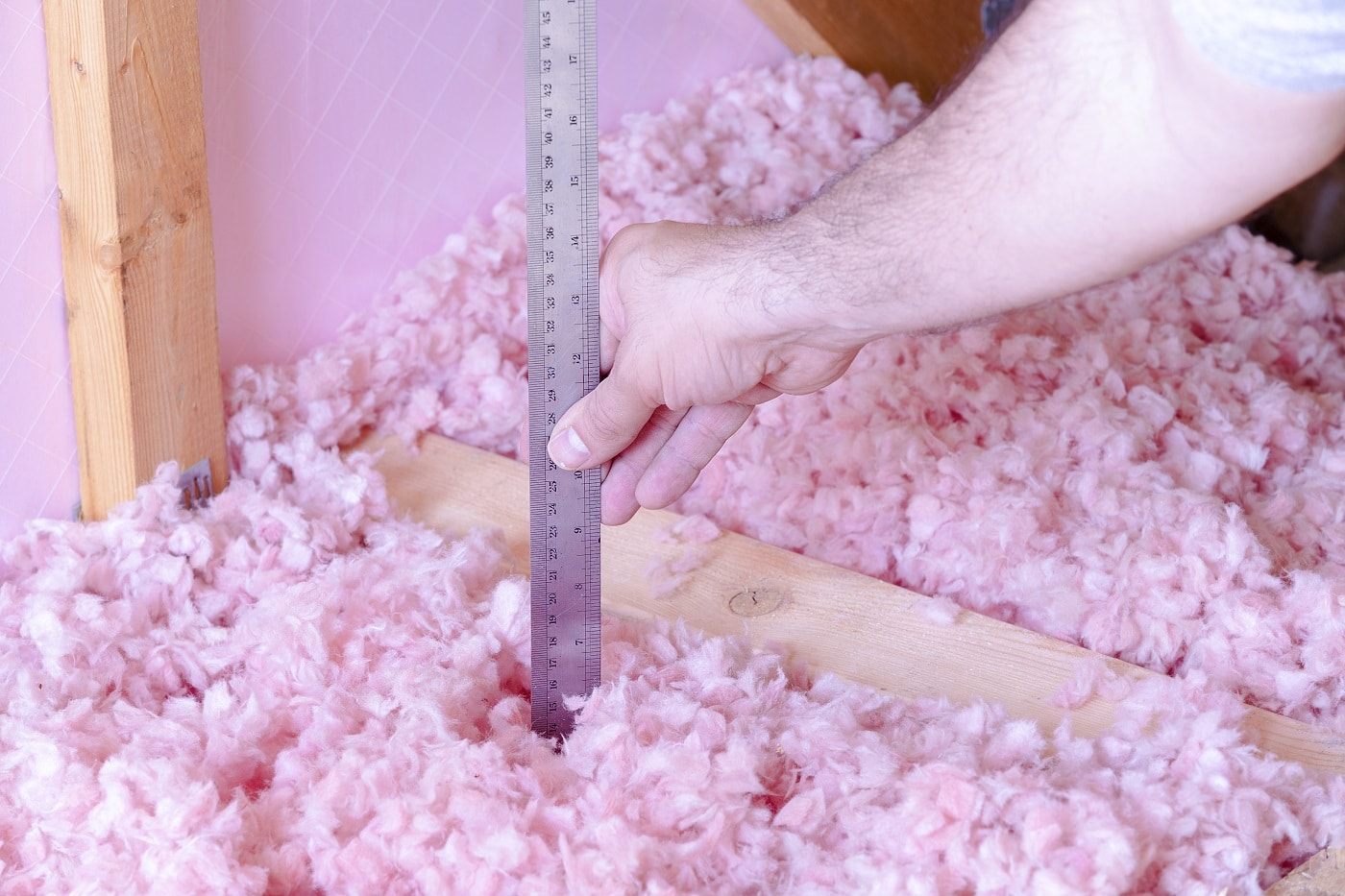 Worker measuring the depth of blown-in insulation in an attic