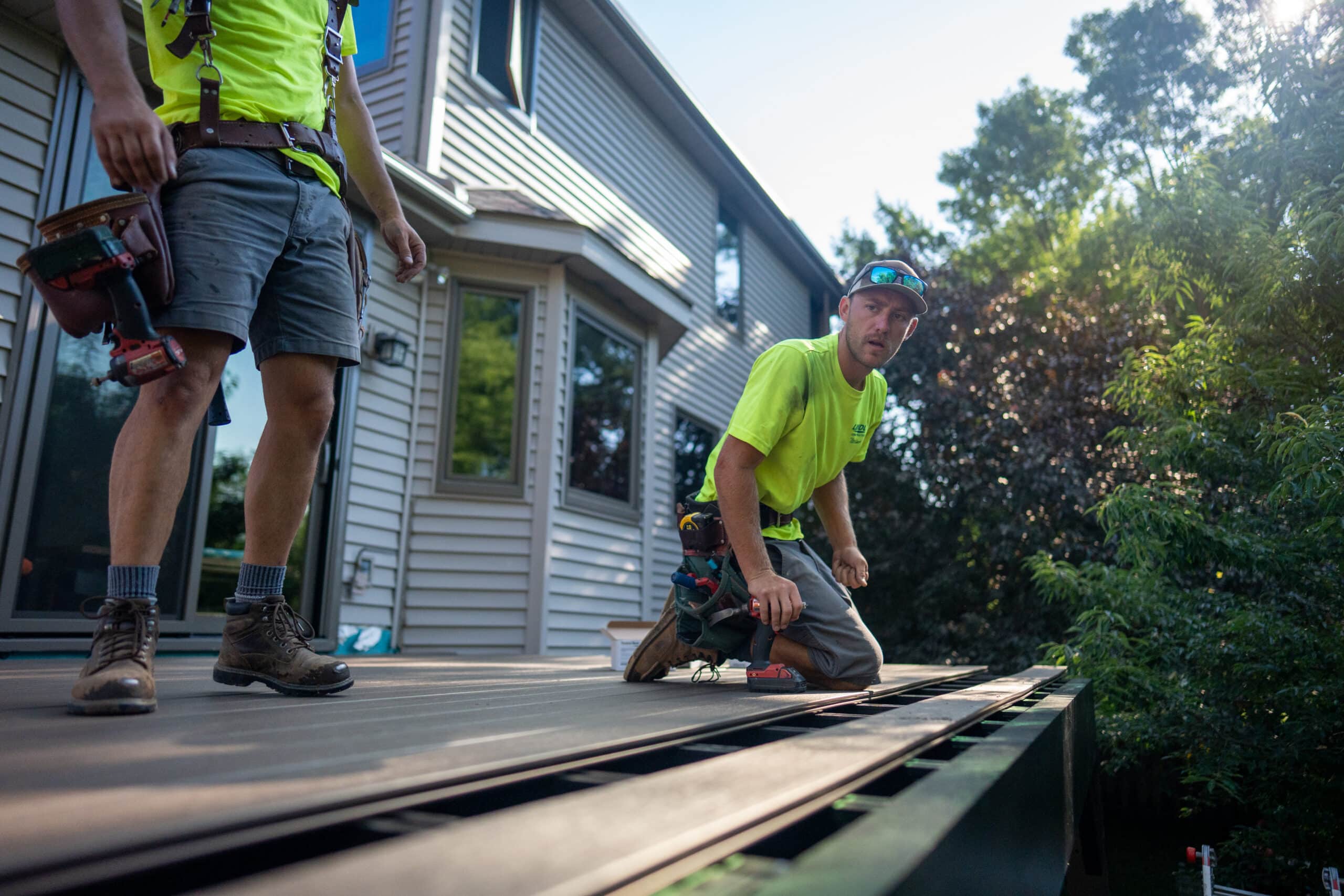 Two Lindus Construction craftsmen kneeling on an elevated deck while installing TimberTech AZEK® decking at a home in Eden Prairie, MN.